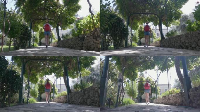戴着帽子和红色背包的旅行者旅游妇女探索希腊科孚岛上的Achillion宫的花园，慢动作