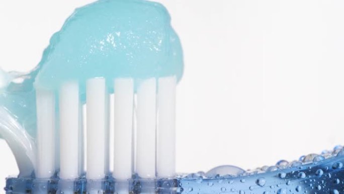 牙刷和牙膏。在蓝色牙刷上慢慢挤压白色背景上的蓝色牙膏。宏视图和慢动作视图