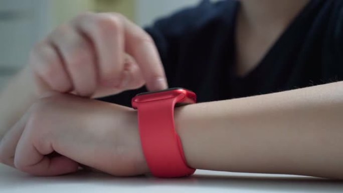 青少年特写手腕上的红色时尚智能手表。男孩在可穿戴设备的屏幕上用手指点击并滚动。