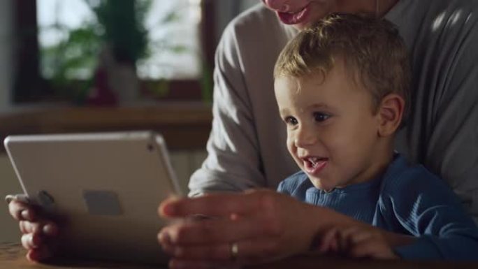 小男孩使用数字平板电脑拍摄的真实照片，与母亲坐在家里在互联网上观看教育视频。喜欢互动媒体和技术的可爱