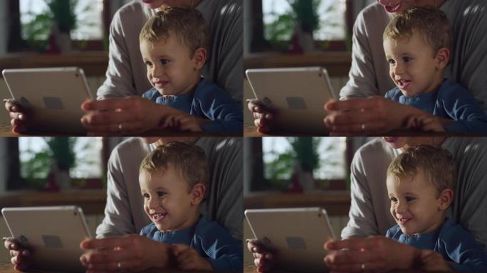 小男孩使用数字平板电脑拍摄的真实照片，与母亲坐在家里在互联网上观看教育视频。喜欢互动媒体和技术的可爱