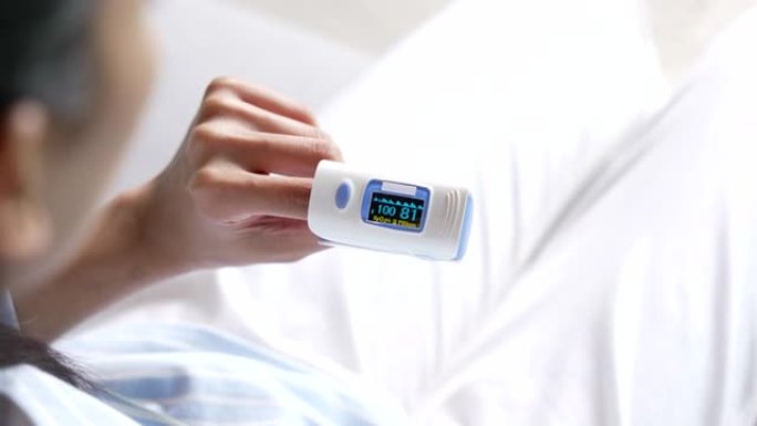年轻的亚洲妇女在家里使用指尖脉搏血氧仪。使用医疗设备测量氧气水平的年轻女子。