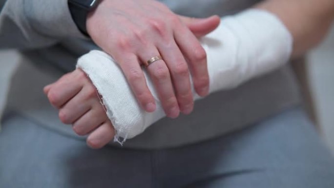 手臂上有石膏的人。骨折时手自我运动的困难。断指手的痛苦沉重动作特写。