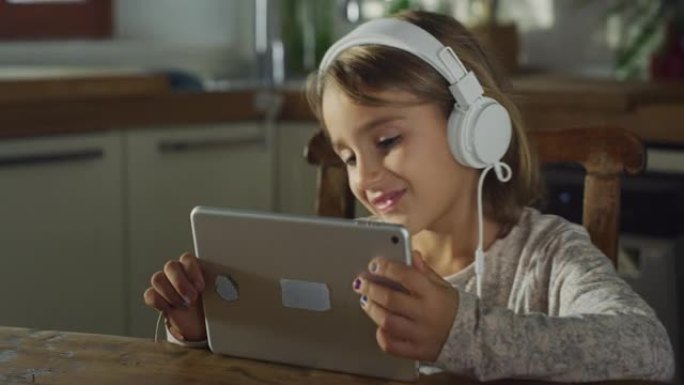 小女孩在数字平板电脑上观看孩子们的歌曲，通过耳机收听和跳舞的真实镜头。厨房里的女学生享受着周末的早晨