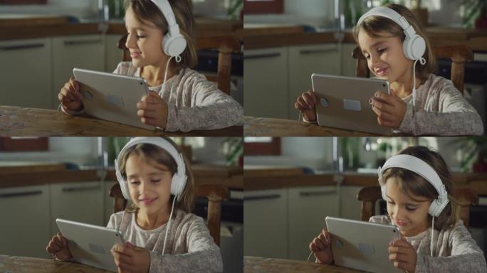 小女孩在数字平板电脑上观看孩子们的歌曲，通过耳机收听和跳舞的真实镜头。厨房里的女学生享受着周末的早晨