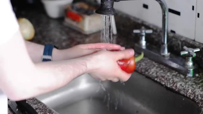 男人洗红色的灯笼椒，绿色的灯笼椒和洋葱，准备午餐