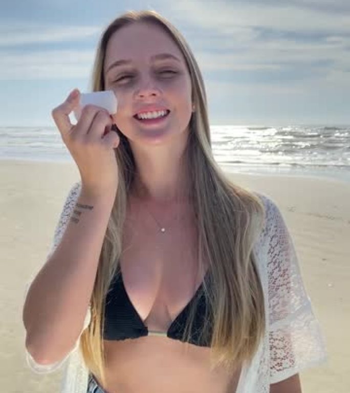 海滩上的白人金发女孩应用无化学有机和素食矿物防晒霜。提到海滩，夏季有黄色和橙色。有太阳的海浪。