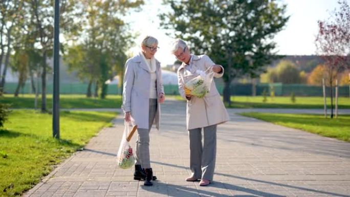 两名资深女性朋友拿着杂货袋在公园里散步