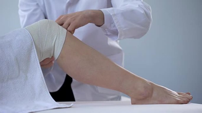 创伤专家在扭伤的患者腿部使用绷带，锻炼受伤