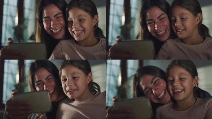 小女孩与母亲一起使用智能手机与家人坐在厨房里与家人进行视频通话的真实照片。女人和她的女儿挥舞着问候，