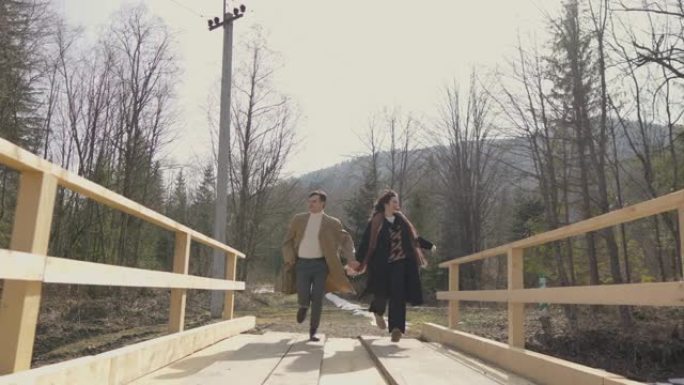 男孩和女孩在山上河上的木桥上奔跑。快乐无忧无虑的年轻夫妇，男人和女人玩得开心，浪漫而积极地休息，快乐