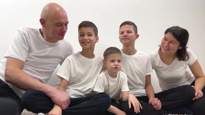 大家庭的交流3个兄弟和父母坐在中心小男孩4年试图在白色背景上穿着白色t恤欢呼友好的家庭爱和平幸福