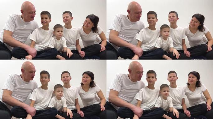 大家庭的交流3个兄弟和父母坐在中心小男孩4年试图在白色背景上穿着白色t恤欢呼友好的家庭爱和平幸福