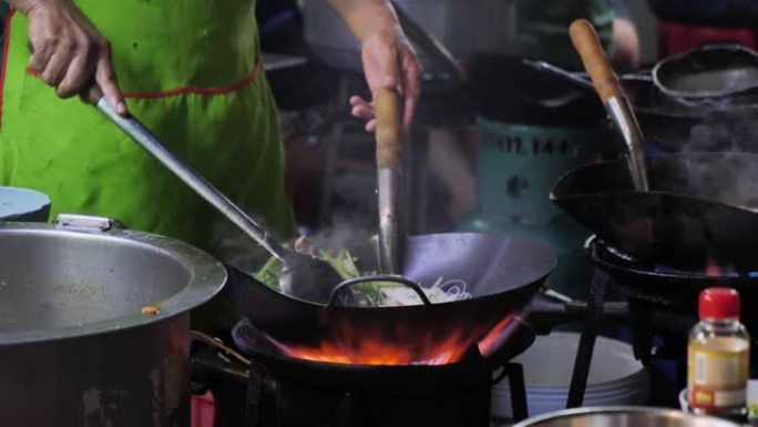 曼谷唐人街的街边炒锅大火。库克晚上在泰国Yaowarat路美食街市中心的马路上向外面的蔬菜燃烧热油。