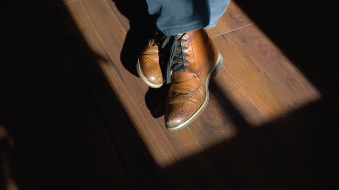 一个穿着牛仔鞋的男人的腿在被光线照亮的木地板上。