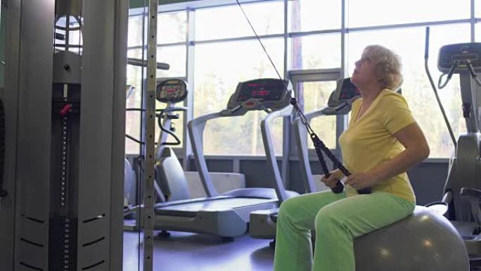 老年妇女在健身房的训练设备上进行拉高运动