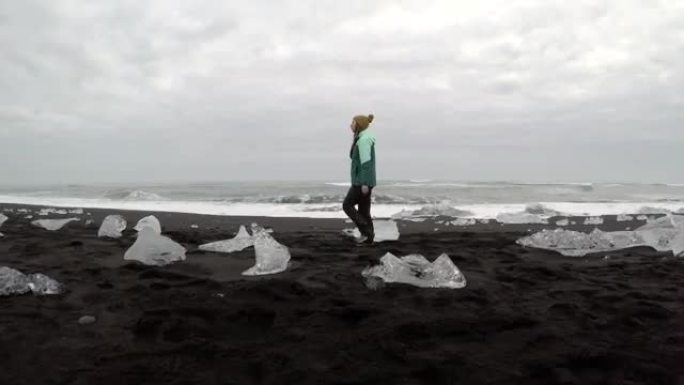 女人在黑沙滩上的冰山中行走