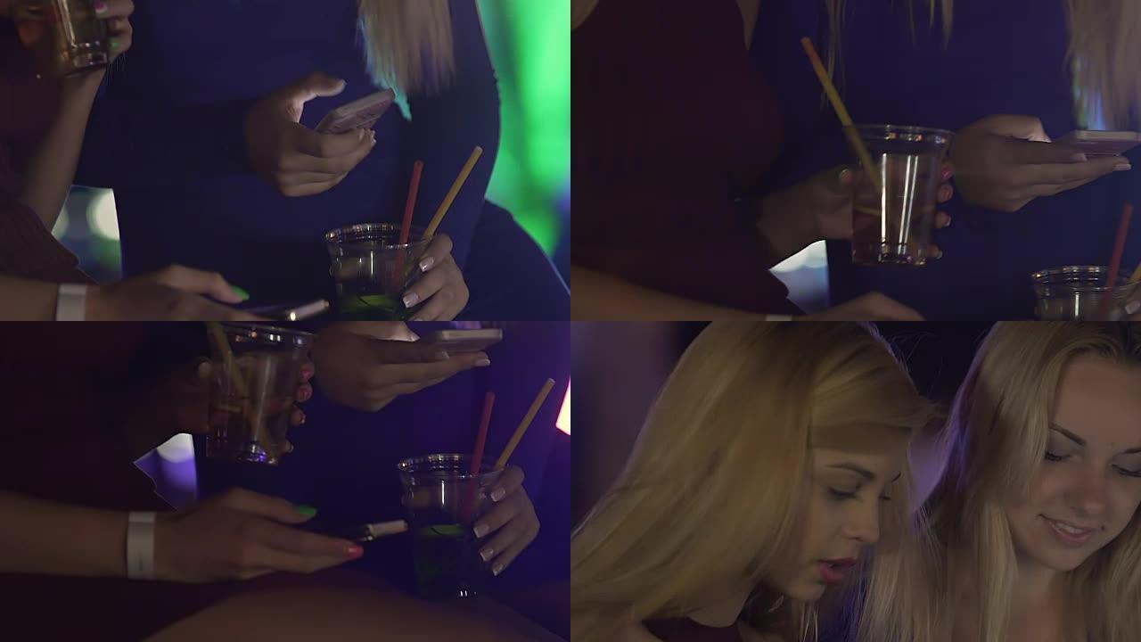 美丽的年轻女性在喝酒时使用手机与朋友社交