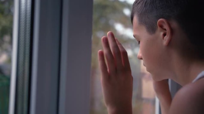 一个悲伤的男孩的肖像看着窗外，孤独，思考，移动相机，电影拍摄