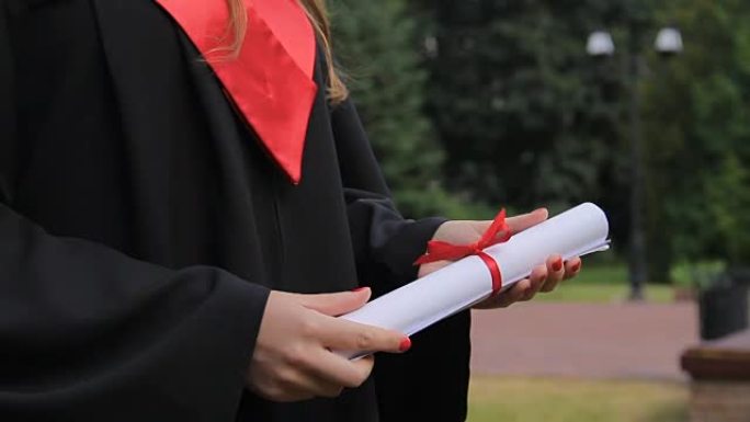 穿着学术服装的年轻女子拿着文凭，享受毕业典礼