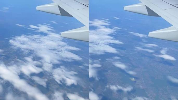 飞机窗口视图，云上，垂直视频。飞越云层的飞机机翼。从高度看地面。