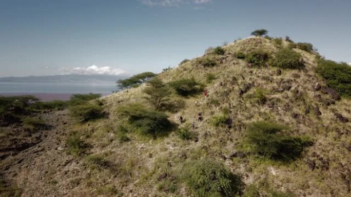 一群徒步旅行的游客在东非攀登一座绿山的4k无人机视图。