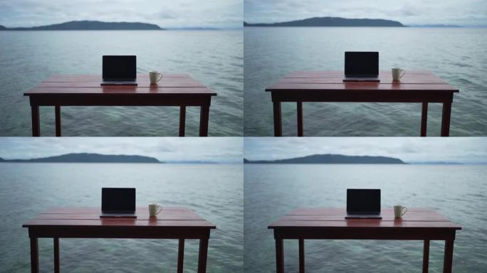 在靠近水域边缘的甲板上的长凳和桌子上的笔记本电脑的视图