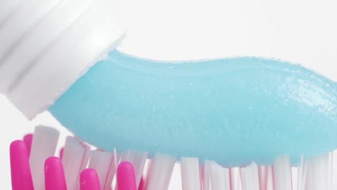 牙刷和牙膏。粉红色牙刷刷毛的宏观视图，白色背景上挤压着蓝色牙膏。慢动作