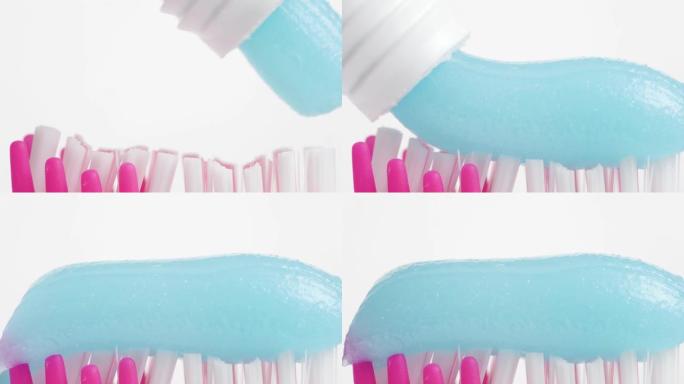 牙刷和牙膏。粉红色牙刷刷毛的宏观视图，白色背景上挤压着蓝色牙膏。慢动作