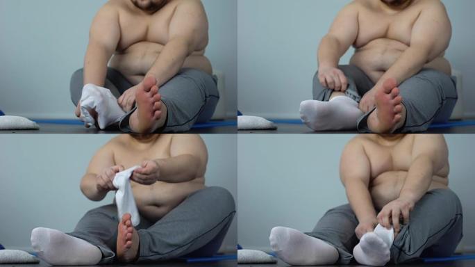 肥胖的腹部男人坐在地板上穿袜子，超重问题，肥胖