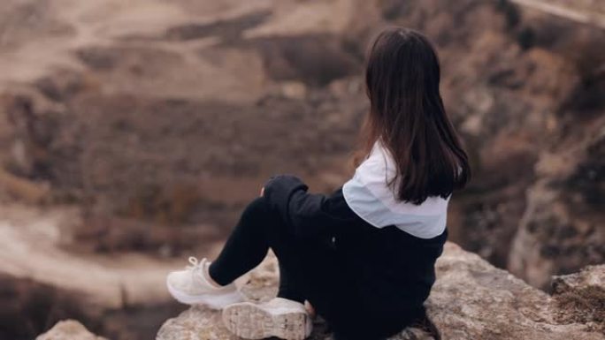 年轻微笑迷人的女游客坐在峡谷岩石的边缘，享受令人惊叹的景色和空间，冥想，吸收大自然的强大能量，做梦和
