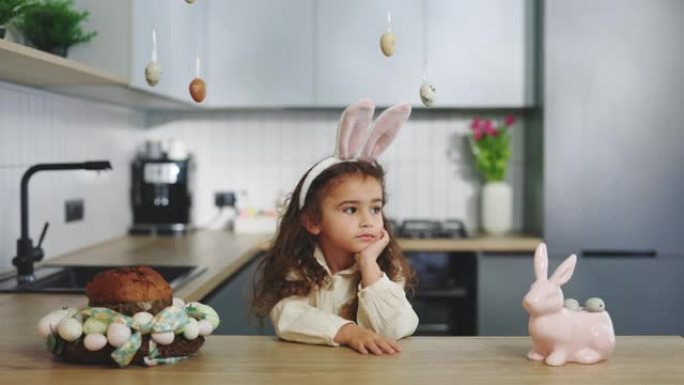 悲伤的复活节小女孩独自坐在装饰好的厨房里。失望的孩子。孩子在春节期间感到不开心。复活节假期。