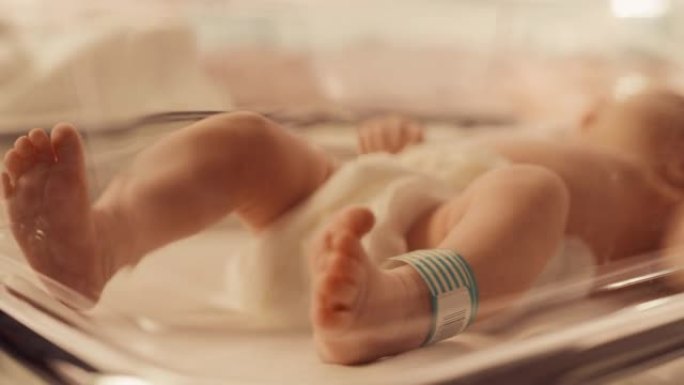 可爱的高加索新生婴儿躺在产科医院的摇篮里。一个小小的顽皮和精力充沛的孩子的肖像，腿上有名字ID标签。
