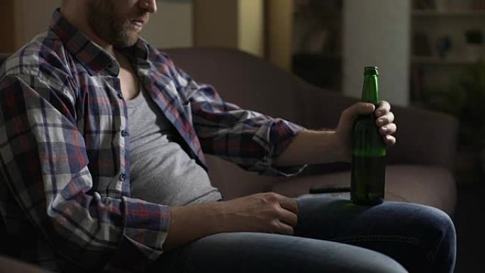 沙发上不整洁的男性喝啤酒，严重叹息，问题和沮丧