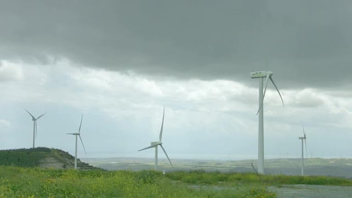 在灰蒙蒙的天空下，在绿色领域旋转的风力涡轮机