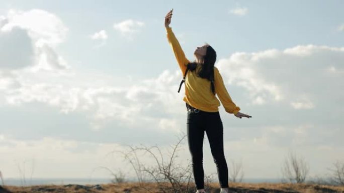 背着背包的女徒步旅行者试图在山上捕捉手机的信号，爬上最高的岩石，但没有信号