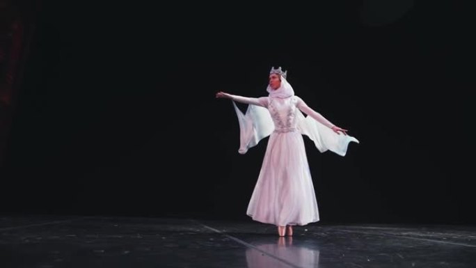 优雅，勤奋的芭蕾舞演员在黑色背景上表演美丽的芭蕾舞元素。风吹着她漂亮的白色西装。慢动作。