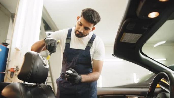 年轻英俊的集中大胡子男人使用清洁刷和清除汽车空调通风格栅上的灰尘。汽车细节和代客概念。汽车细节和代客