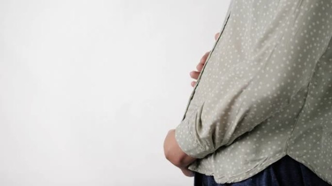 怀孕。白色背景的女人小心翼翼地抚摸着她的腹部。特写和慢动作