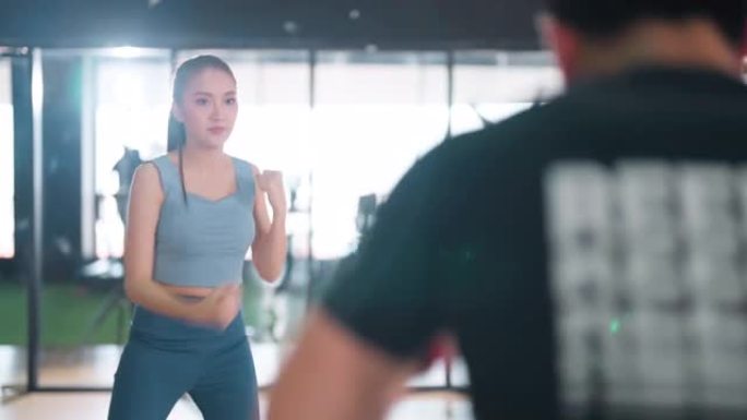 在训练课上进行健身武术锻炼时，年轻女性朋友在拳击中进行身体搏击。男教练在健身馆展示运动