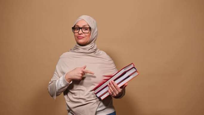 愉快的阿拉伯穆斯林妇女，头上盖着头巾，与米色背景上的书籍合影