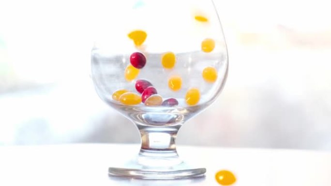糖衣慢慢掉进玻璃杯里。红黄色药丸，糖果被倒入白色背景上的透明碗中。文本的位置。