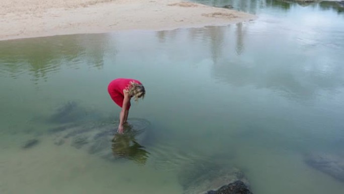 女人涉水进入清澈的溪流，抚摸水面