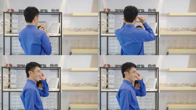 微笑的亚洲年轻人在眼镜店试戴新眼镜。帅哥戴新眼镜看相机眼镜店眼科门诊选择眼镜概念