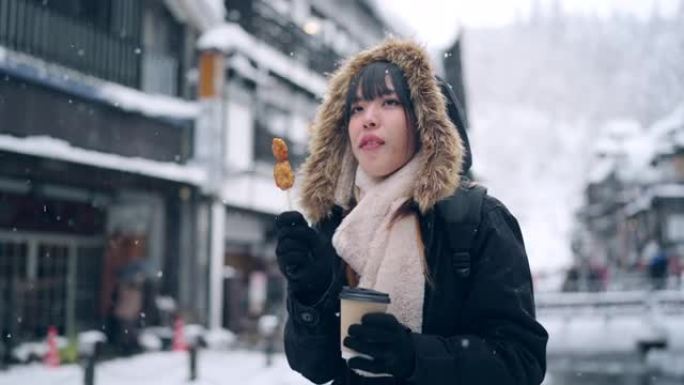 4K亚洲妇女在下雪天在Ginzan onsen地区旅行时吃街头食物和喝热咖啡。