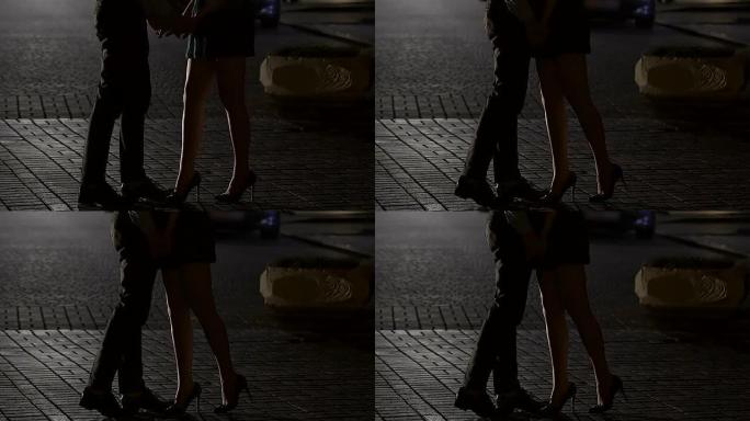 女人和男人站在夜街上，手牵手，亲吻，双腿射击