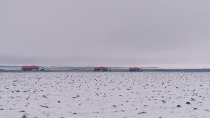 卡车司机穿着红色和白色的油罐车在路上行驶。冬。阴天。雪场。从无人机上看。全景视图。4K