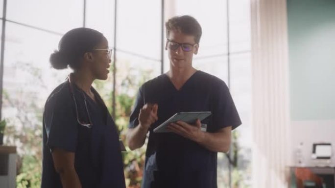 两名年轻医生站在医院的医疗机构里，在平板电脑上交谈和分享信息。拥有多元化多民族专业医护人员的现代化医