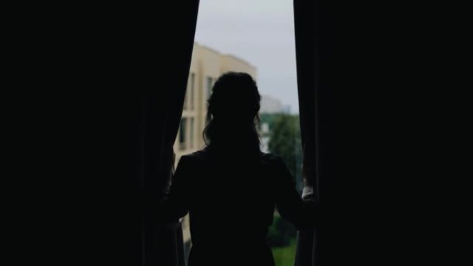 女孩站在窗前，推开她面前的窗帘。可以看到街道的景色