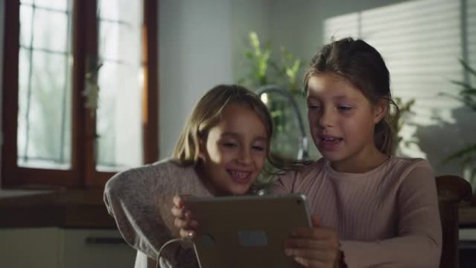 两个小女孩在数字平板电脑上观看孩子们的歌曲，一起唱歌和跳舞的真实镜头。厨房里的两个姐妹一起度过周末。